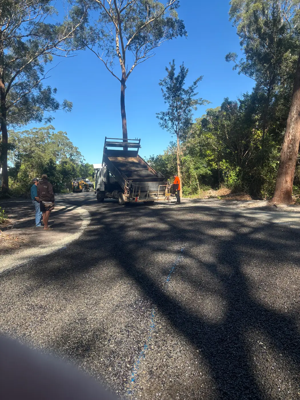 Tipper truck delivering asphalt on a tree-lined road resurfacing job