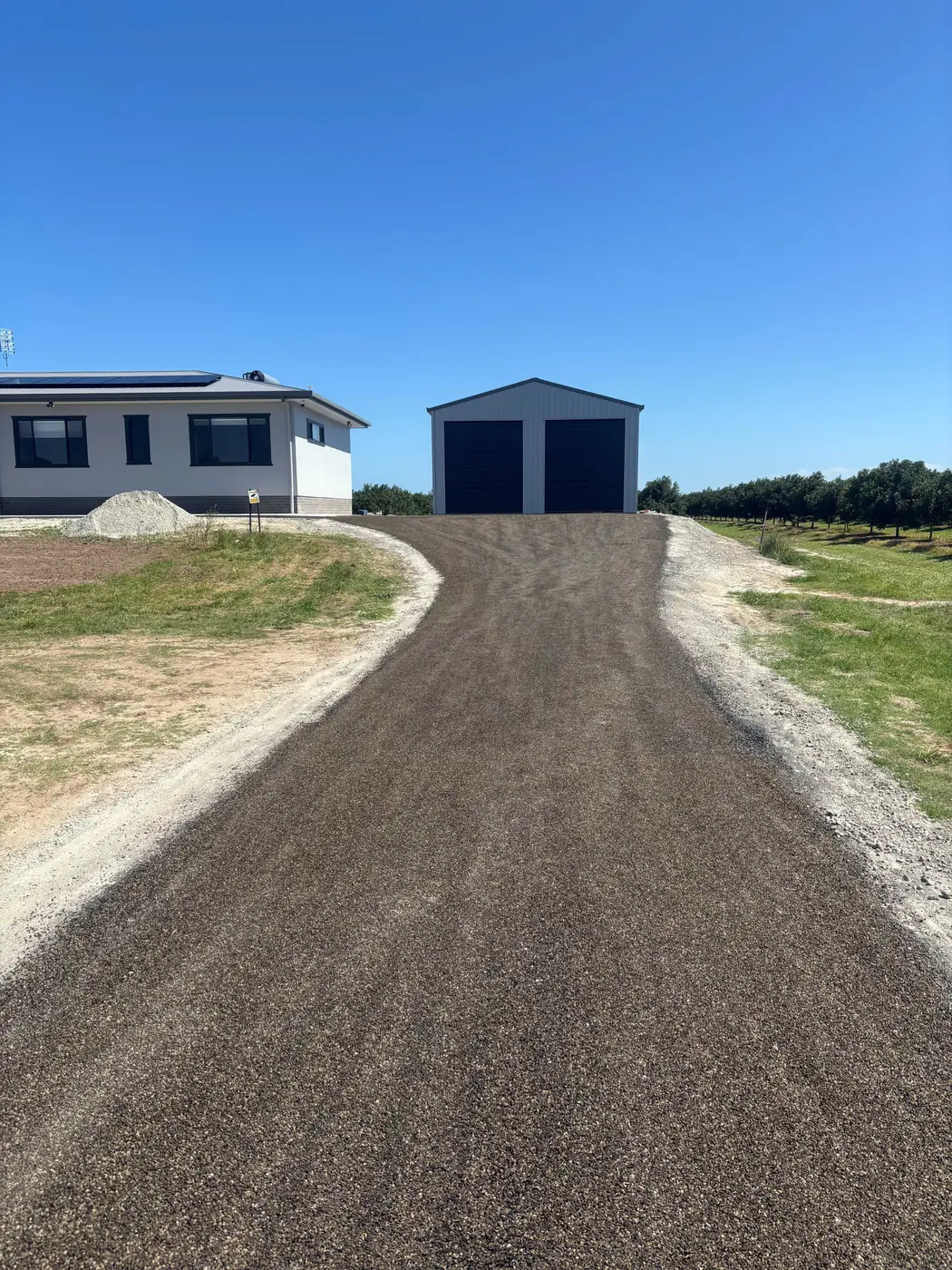 Completed bitumen driveway leading to a rural shed and house