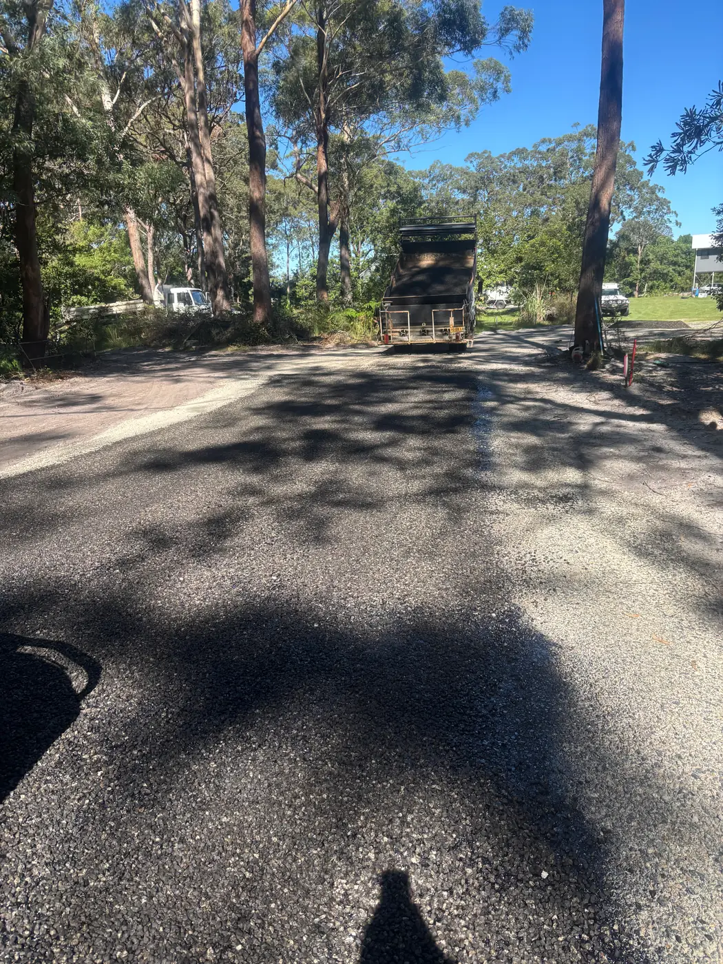 Completed asphalt resurfacing on a shaded bush road