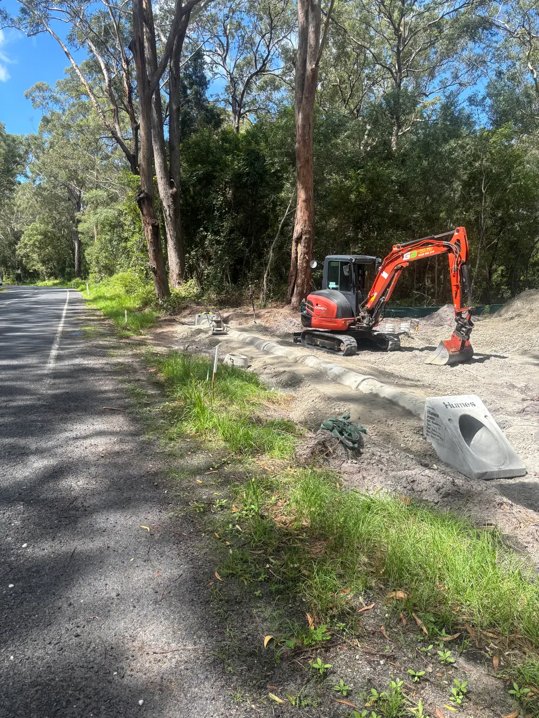 Mini excavator setting a roadside drainage pit on a rural road