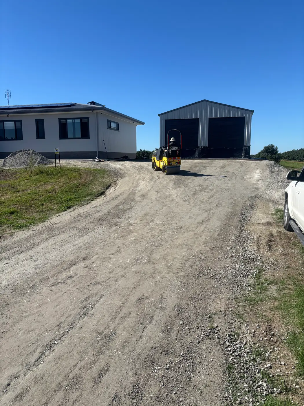 Roller preparing a rural driveway base to a shed